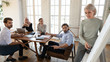 © fizkes - Focused multiethnic business people listen old businesswoman coach give presentation