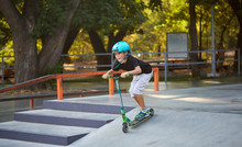 A Boy On A Scooter And In Protective Helmet Do Incredible Stunts In Skate Park. Extreme Jump. The Concept Of A Healthy Lifestyle And Sports Leisure