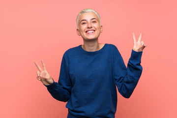 Teenager girl with white short hair over pink wall showing victory sign with both hands