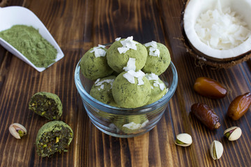 Wall Mural - Energy balls with  matcha powder, pistachios, dates  and coconut chips in the glass bowl  on the brown  wooden background. Closeup.