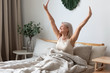 Happy mature woman stretching in bed waking up happy concept