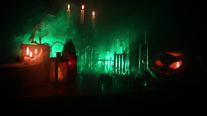 Wizard's Desk. Horror Halloween concept. Magic potions in bottles on wooden table with books and candles. Halloween still-life background with different elements on dark toned foggy background. Select