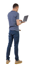 Wall Mural - Back view of a man who is standing with a laptop.