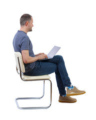 Canvas Print - Side view of a man who sits on a chair with a laptop.