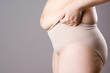 Fat woman in corrective panties, flabby belly after pregnancy, overweight female body on gray background