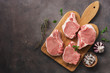 Raw pork slices on a cutting board with spices and herbs, dark rustic background. Top view, flat lay, copy space.