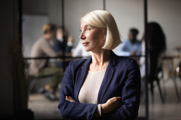 Thoughtful old businesswoman ceo looking through window thinking of leadership