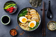 Asian noodle soup, ramen with chicken, tofu, vegetables and egg in black bowl. Slate background. Top view.