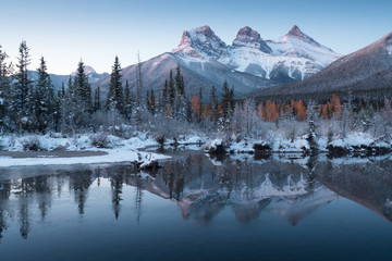 Wall Mural - first snow almost near perfect reflection of the three sisters peaks in the bow river. canmore in ba