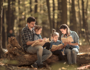 Family together reading books in the forest .