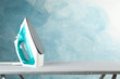 Iron on ironing board against blue background, space for text