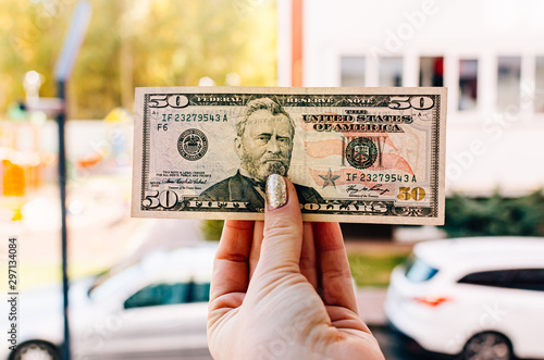 Fotografía Female hand holds 100 dollar bill against the background of the street