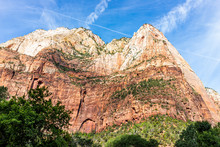 Low Angle View Of Red Orange Zion National Park Cliffs Desert Landscape During Summer Day With Tall High Rock Formations And Green Plants