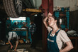 © _KUBE_ - The concept of small business, feminism and women's equality. A young female auto mechanic wearily wipes sweat from her forehead