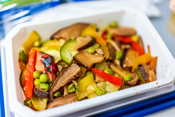 Healthy vegan asian stir fry food vgml hot meal on airplane flight tray with mushrooms, teriyaki noodles and vegetables closeup