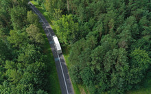 Aerial Drone Perspective View On White Truck With Cargo Trailer Riding Through The Forest On Curved Asphalt Road