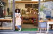 © marvent - Smiling young African American barista leaning against a cafe door