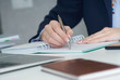 © cameravit - Young businesswoman writing in notepad while sitting at the office. Female hands holding a pen and making notes close up.