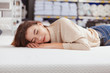 © Ihor - Young beautiful woman smiling with her eyes closed, lying on orthopedic mattress at furniture store