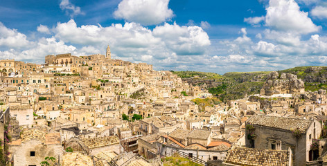 Aerial panoramic view of historical centre Sasso Caveoso of old ancient town Sassi di Matera with rock cave houses, blue sky white clouds, UNESCO World Heritage Site, Basilicata, Southern Italy