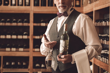 Wall Mural - Sommelier Concept. Senior man standing with bottle and wine glass upside down serious close-up