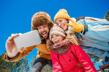 Winter vacation. Family time together outdoors taking selfie on smartphone grimacing to camera playful bottom view