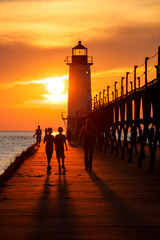 Wall Mural - lighthouse at sunset with silhouette shadows of people