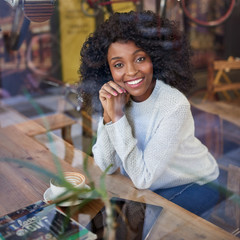 Wall Mural - Young African American woman smiling while sitting in a cafe