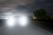 A car driving along a night highway is approaching from the dark and is blinding by the headlights.