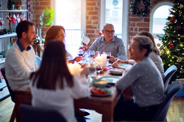 Wall Mural - Family and friends dining at home celebrating christmas eve with traditional food and decoration, all sitting on the table together