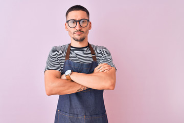 Sticker - Young handsome man wearing employee apron over isolated background skeptic and nervous, disapproving expression on face with crossed arms. Negative person.