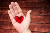 Fototapeta  - heart symbol in the hand of an elderly woman on a blurred wooden background