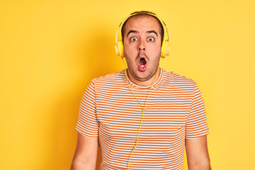 Sticker - Young man listening to music using headphones standing over isolated yellow background afraid and shocked with surprise expression, fear and excited face.