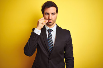 Canvas Print - Young handsome businessman wearing suit and tie standing over isolated yellow background mouth and lips shut as zip with fingers. Secret and silent, taboo talking