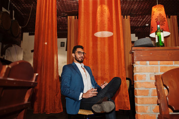 Wall Mural - Handsome well-dressed arabian man with glass of whiskey and cigar posed at pub.