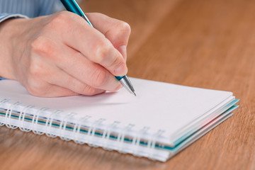 Close up of woman's hands writing in spiral notepad placed on wooden desktop with various items