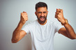 © Krakenimages.com - Young indian man wearing t-shirt standing over isolated white background angry and mad raising fists frustrated and furious while shouting with anger. Rage and aggressive concept.