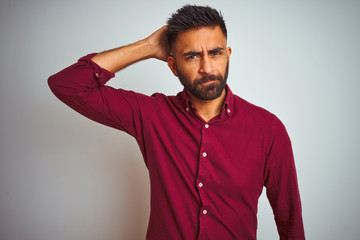 Wall Mural - Young indian man wearing red elegant shirt standing over isolated grey background confuse and wondering about question. Uncertain with doubt, thinking with hand on head. Pensive concept.