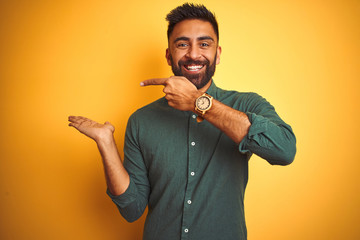 Canvas Print - Young indian businessman wearing elegant shirt standing over isolated white background amazed and smiling to the camera while presenting with hand and pointing with finger.