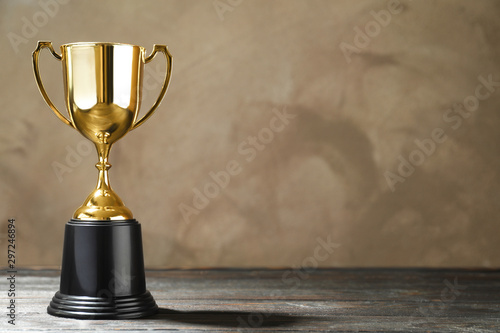Fotomural Golden trophy cup on wooden table against light brown background