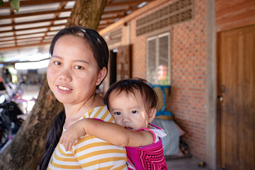 Asian woman carrying her baby girl on back