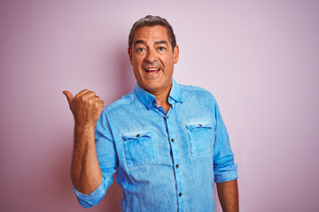 Wall Mural - Handsome middle age man wearing blue denim shirt standing over isolated pink background pointing and showing with thumb up to the side with happy face smiling