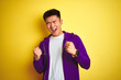 © Krakenimages.com - Young asian chinese man wearing purple sweatshirt standing over isolated yellow background very happy and excited doing winner gesture with arms raised, smiling and screaming for success