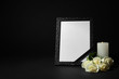 © New Africa - Funeral photo frame with ribbon, white roses and candle on dark table against black background. Space for design