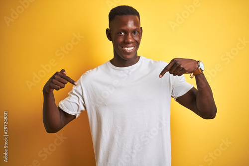 Young african american man wearing white t-shirt standing over isolated yellow background looking confident with smile on face, pointing oneself with fingers proud and happy Poster Mural XXL