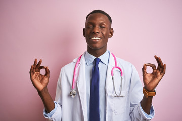 African american doctor man wearing stethoscope standing over isolated pink background relax and smiling with eyes closed doing meditation gesture with fingers. Yoga concept.