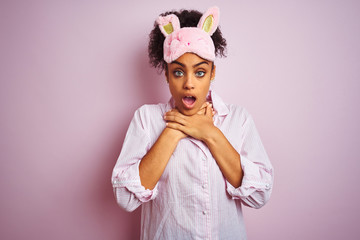 Poster - Young african american woman wearing pajama and mask over isolated pink background shouting suffocate because painful strangle. Health problem. Asphyxiate and suicide concept.