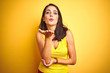 © Krakenimages.com - Young beautiful woman wearing t-shirt standing over yellow isolated background looking at the camera blowing a kiss with hand on air being lovely and sexy. Love expression.