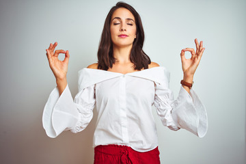 Wall Mural - Young beautiful woman wearing t-shirt standing over white isolated background relax and smiling with eyes closed doing meditation gesture with fingers. Yoga concept.