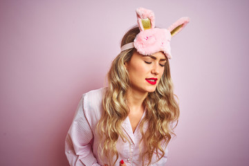 Wall Mural - young beautiful woman wearing pajama and sleep mask over pink isolated background with hand on stoma